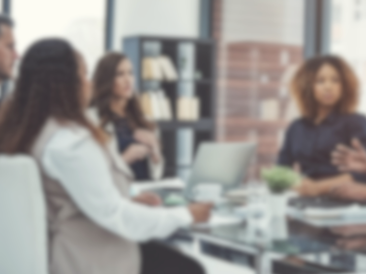 Blurred photo of people sitting at a table in a professional meeting.