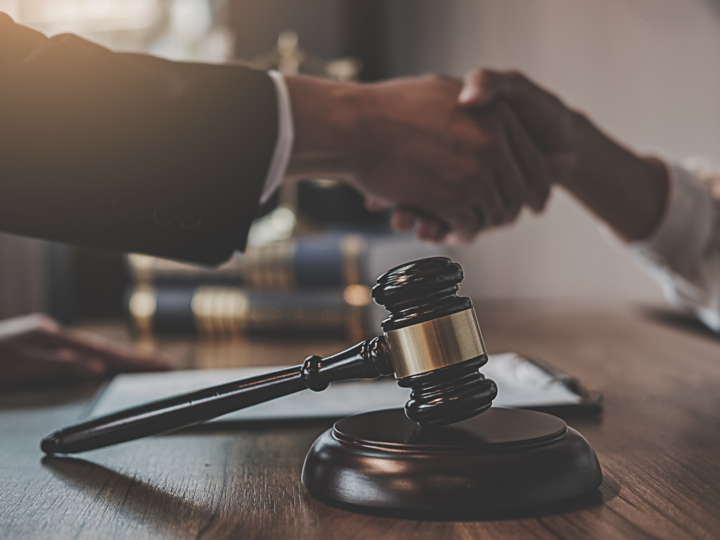 A judge's gavel rests on a desk in front of two people shaking hands.