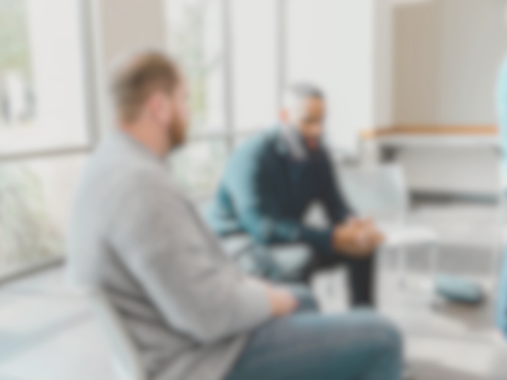 A blurred photo of men sitting in a group therapy setting.